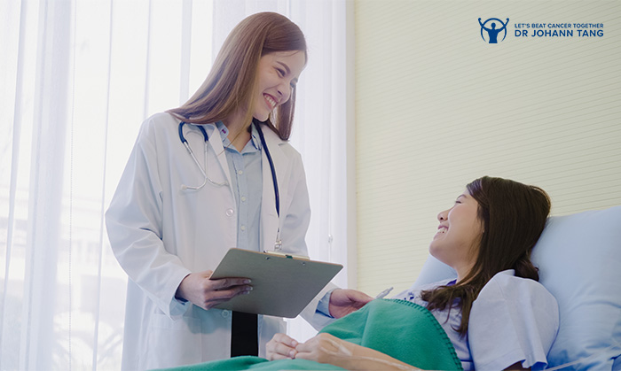 Female oncologist consulting smiling nose cancer patient in hospital bed